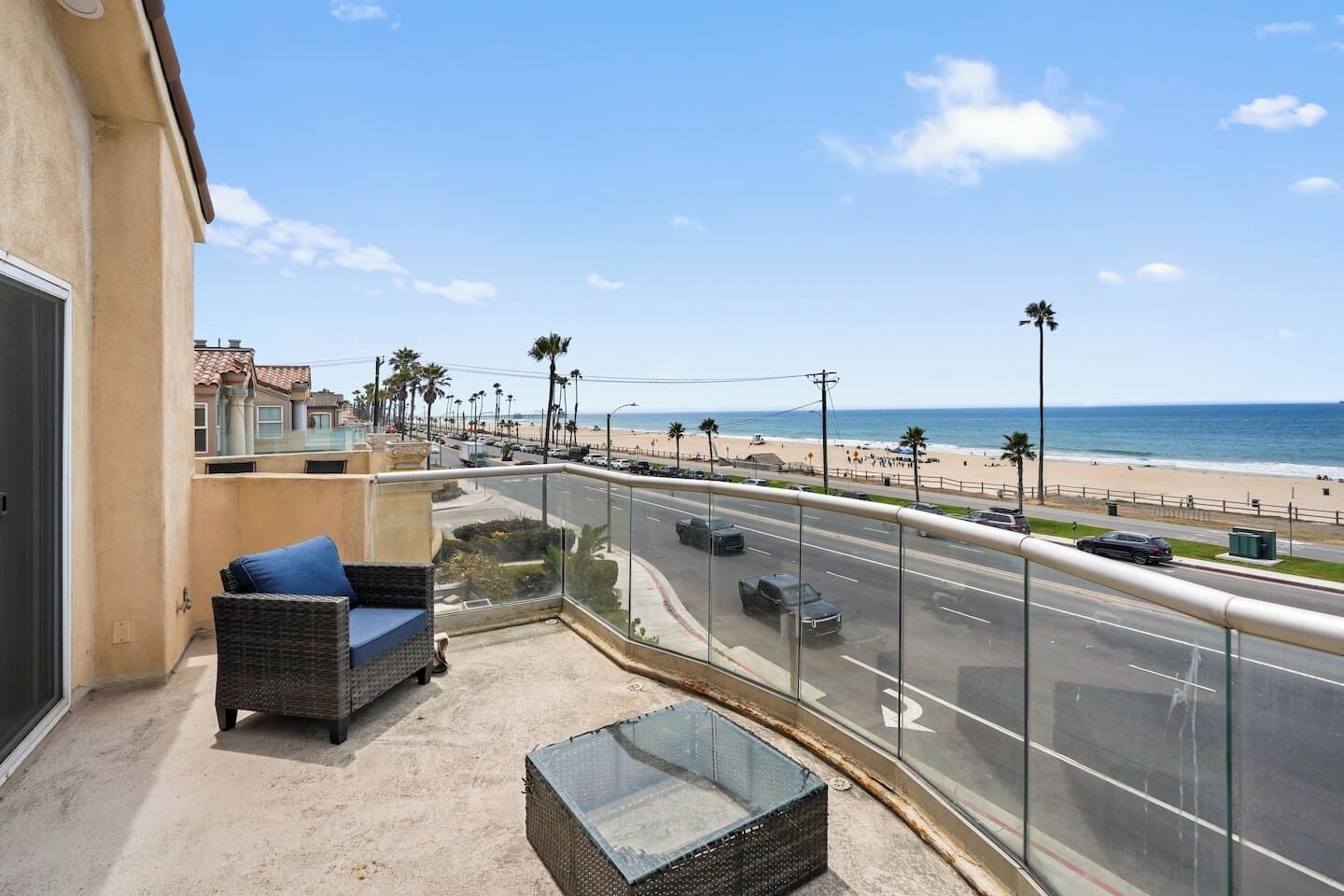 Ein Balkon mit Korbmöbeln, einem Glastisch und Blick auf den Strand und das Meer.