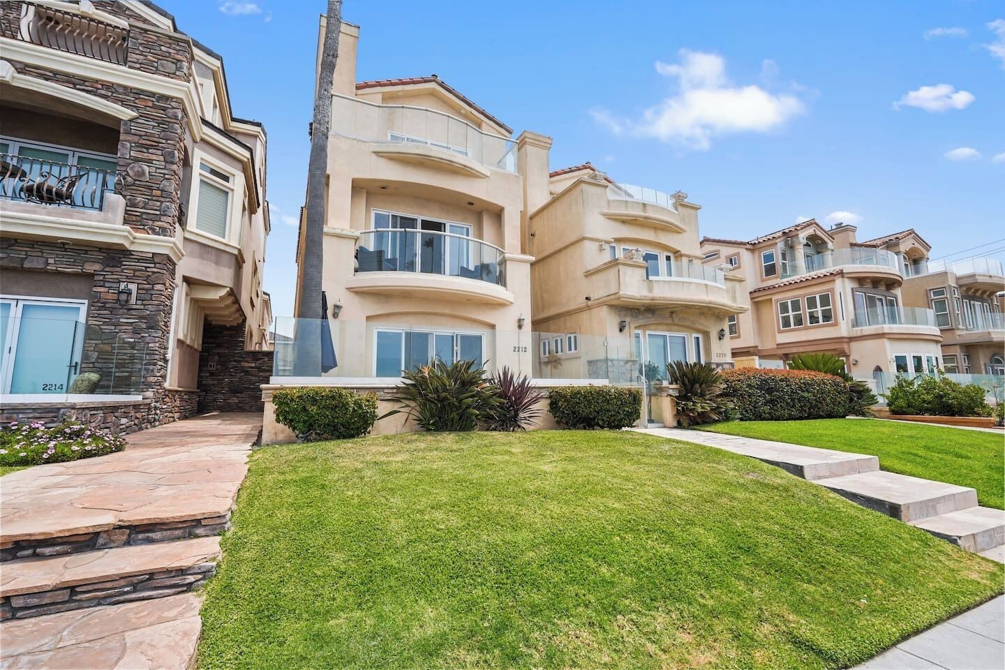 A multi-story residential building with balconies, a stone facade, and a well-maintained lawn.