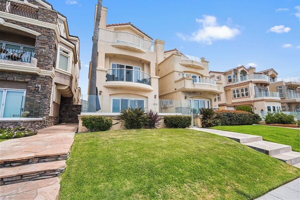 A multi-story residential building with balconies, a stone facade, and a well-maintained lawn. - Beachfront Oasis | 3BR | Ocean Views | Steps 2 HB (Huntington Beach)