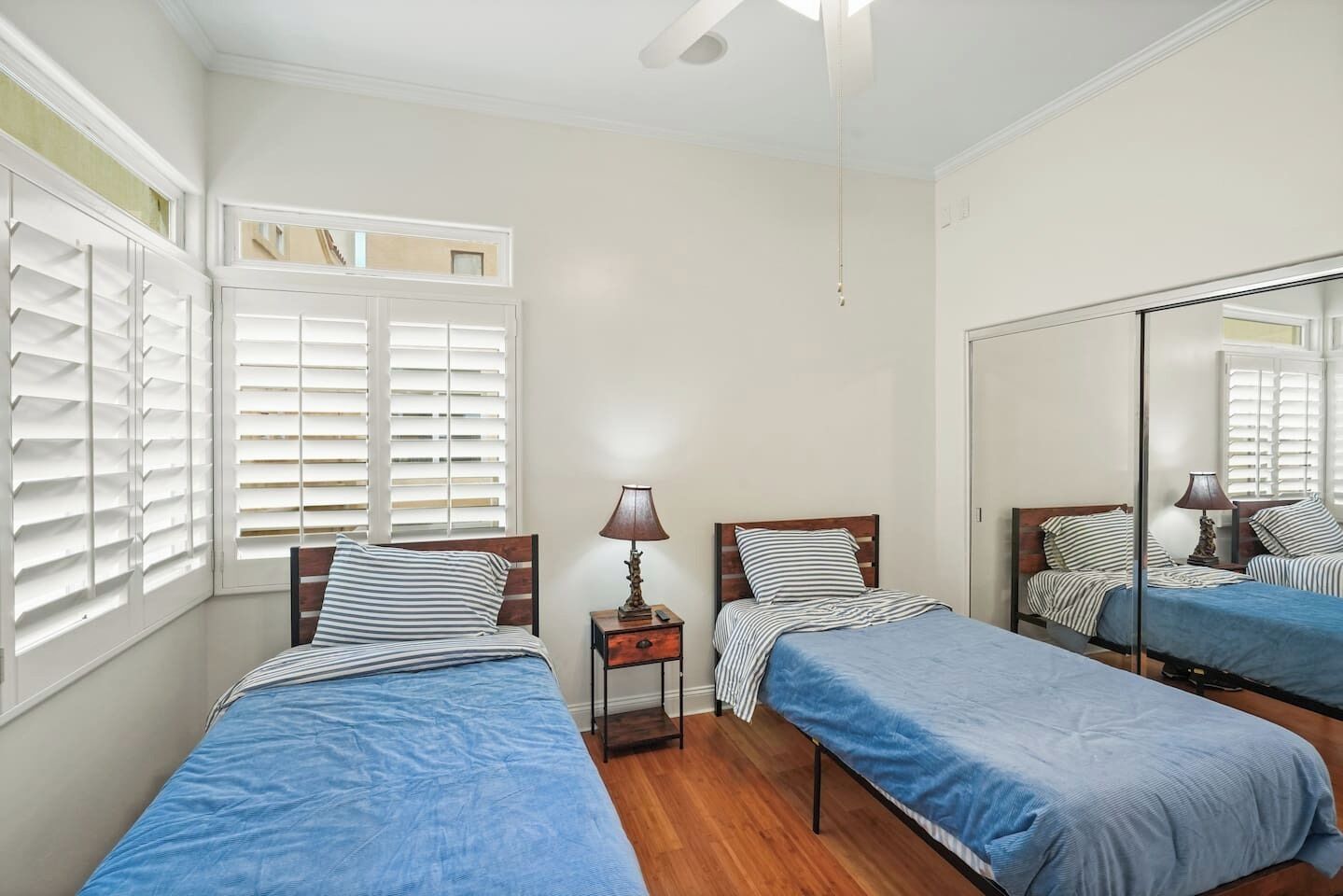 A bedroom with two beds, a mirror, and a window with shutters.