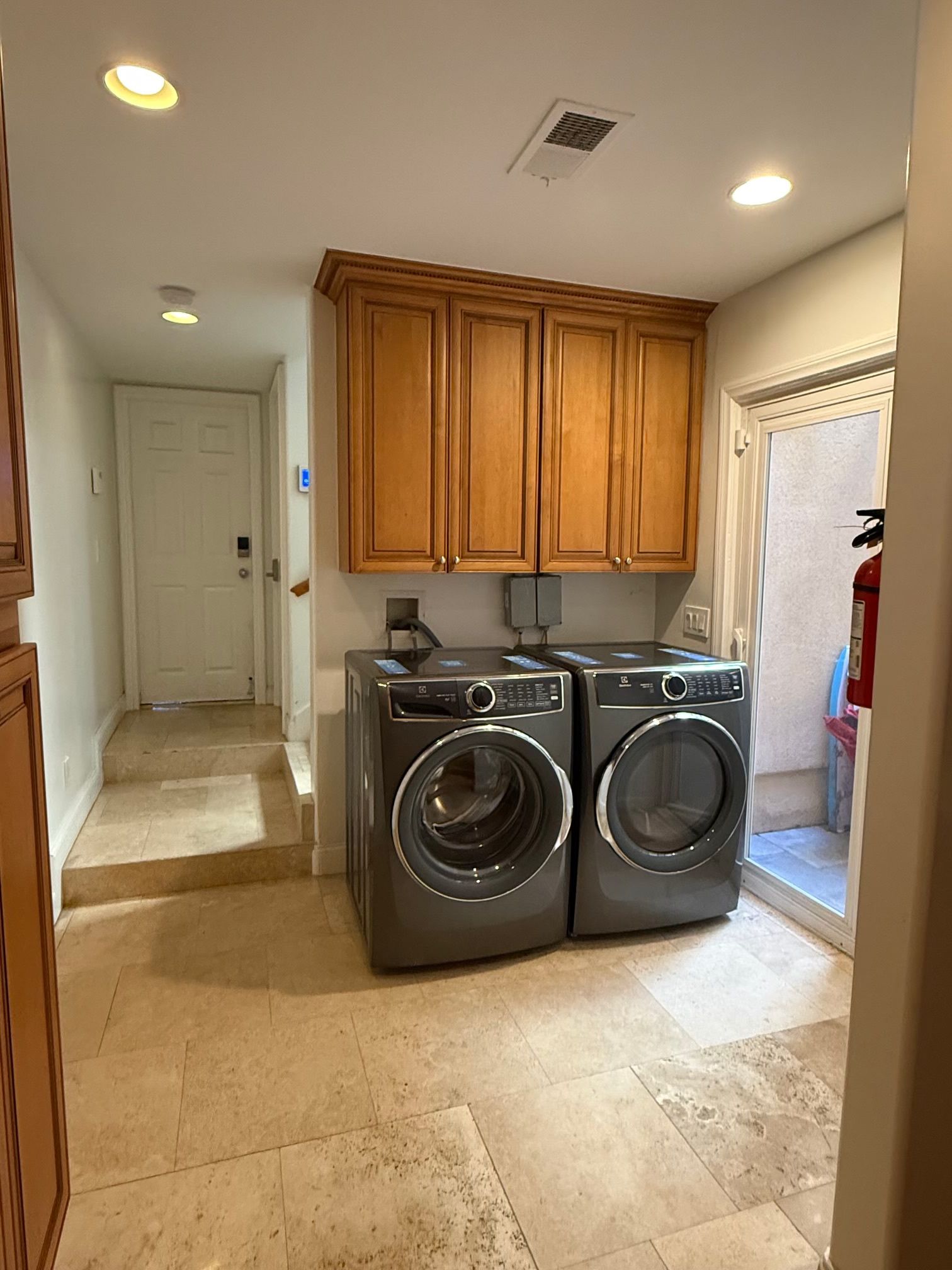 A laundry room with two front-loading washing machines, wooden cabinets above, and a tiled floor.