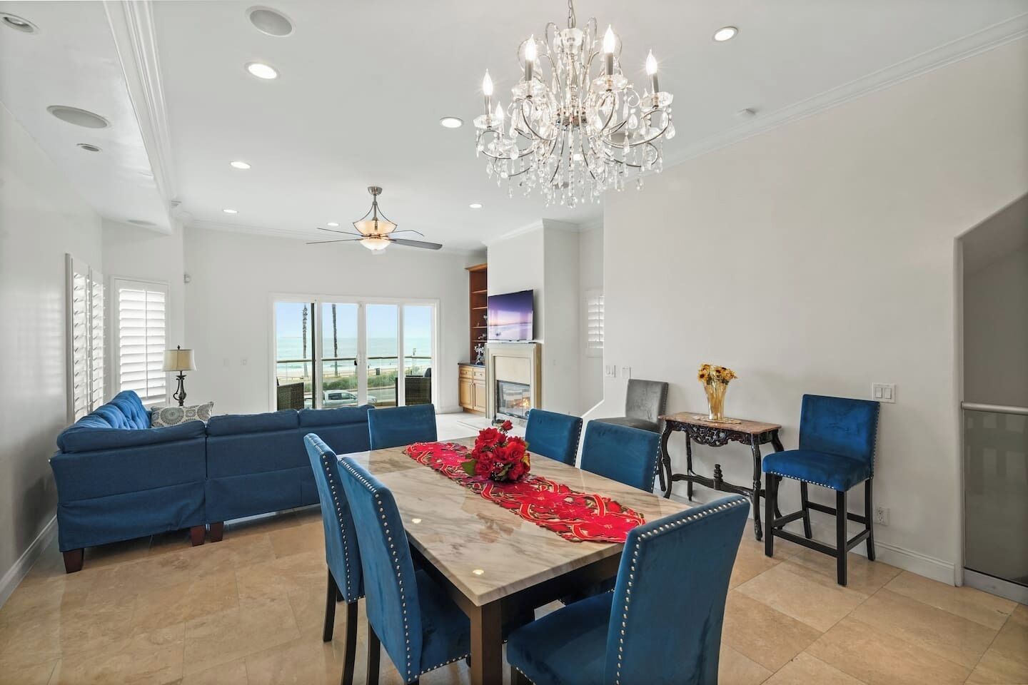 A dining area with a table set for four, blue upholstered chairs, a chandelier, and a ceiling fan.