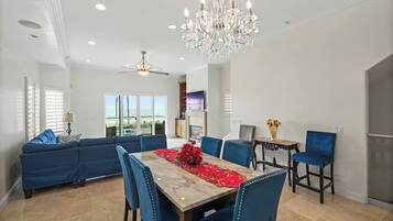 A dining area with a table set for four, blue upholstered chairs, a chandelier, and a ceiling fan.