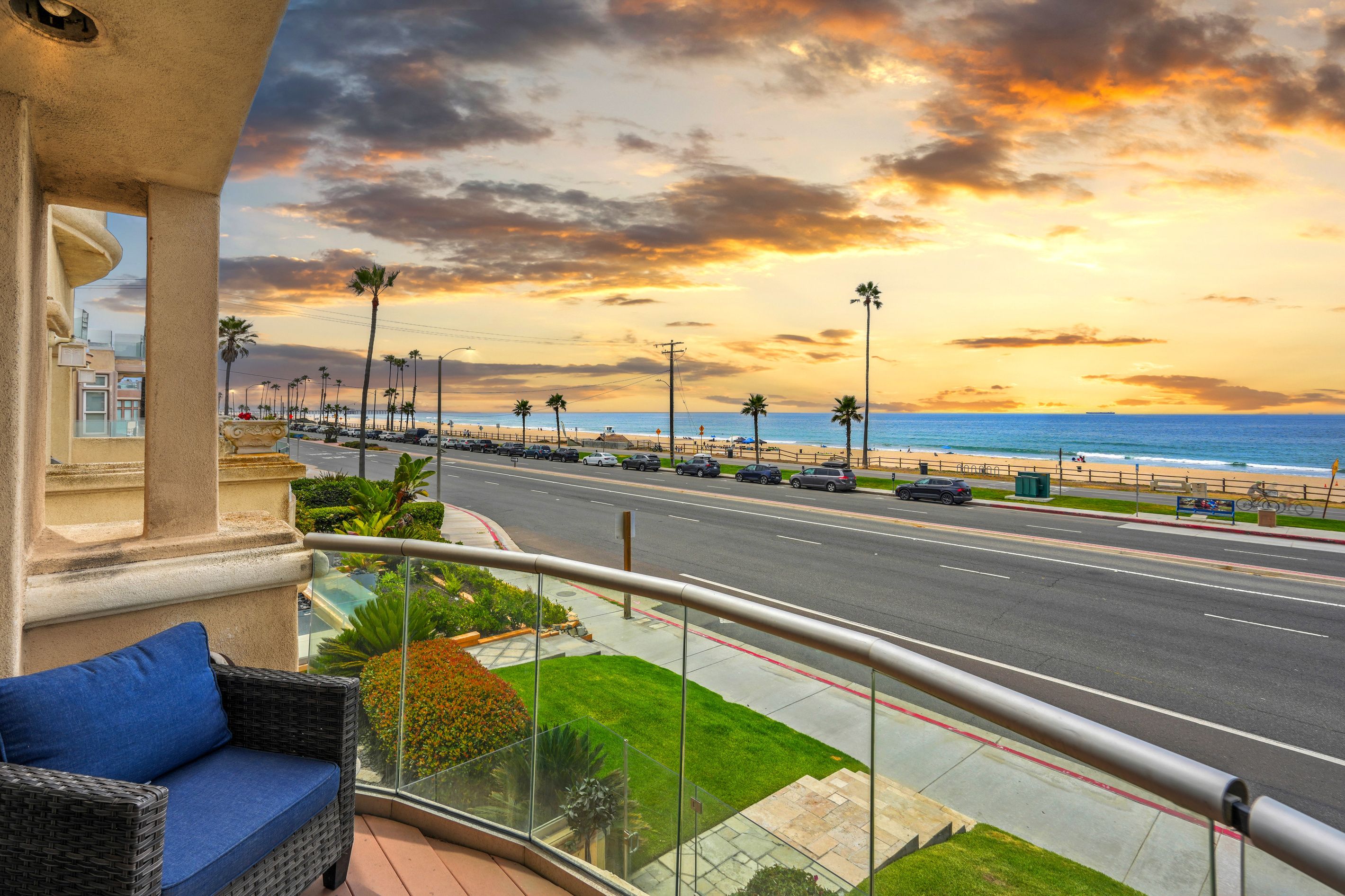 A vibrant sunset sky over the Pacific Ocean seen directly from the private balcony highlights the prime beachfront setting and provides an instantly captivating, colorful focal point.