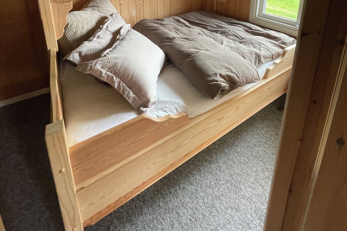 Un lit superposé avec une fenêtre, des murs en bois et un sol recouvert de moquette.