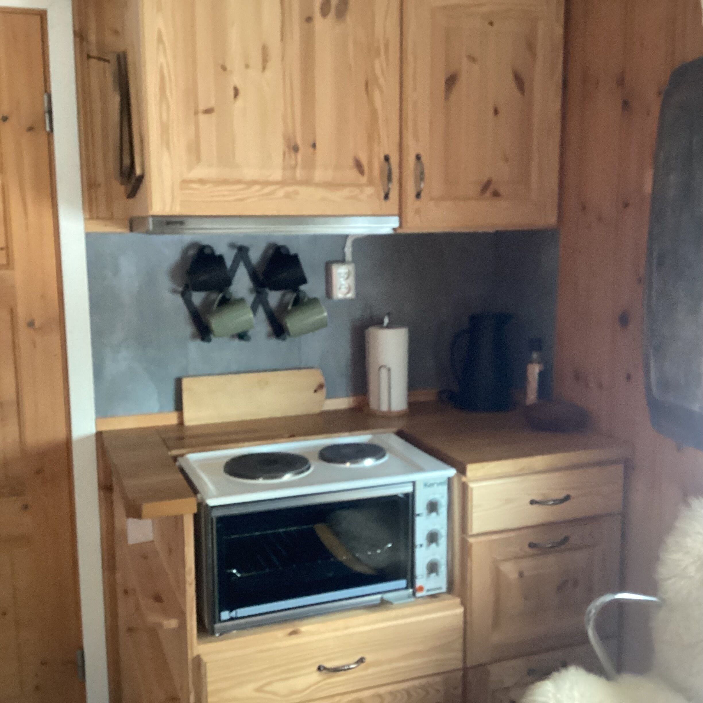 A compact kitchen with wooden cabinets, a built-in oven, a small countertop, and a chair.