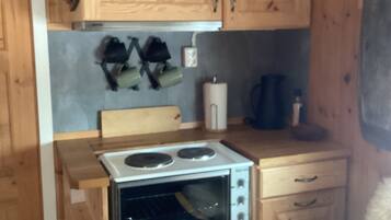 A compact kitchen with wooden cabinets, a built-in oven, a small countertop, and a chair.