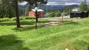 Un campo cubierto de césped con un edificio rojo, un cobertizo negro y una plataforma de madera.