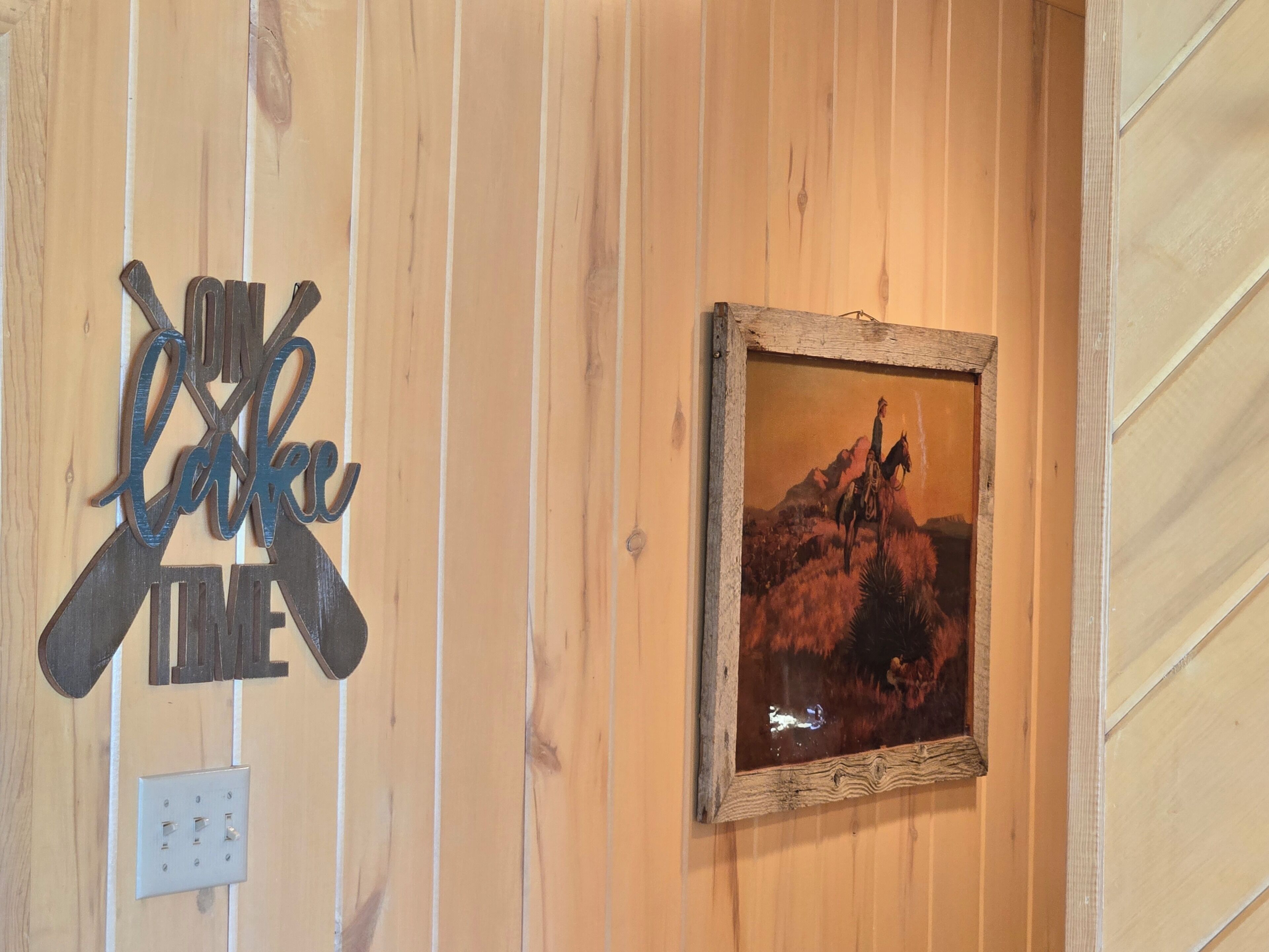 A wooden wall with a framed painting and a metal sign.
