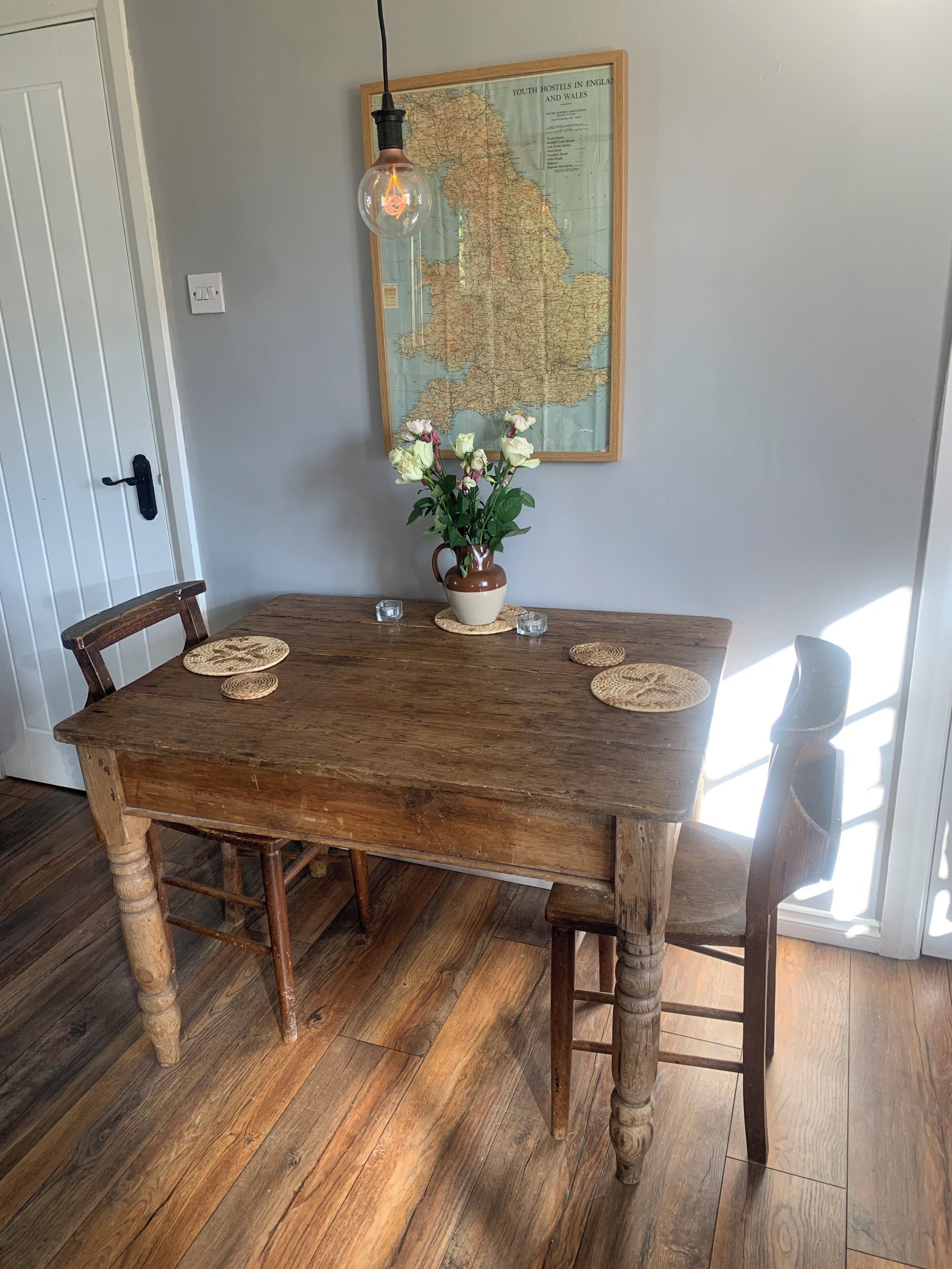 A wooden dining table with chairs, a map on the wall, and a vase with flowers.