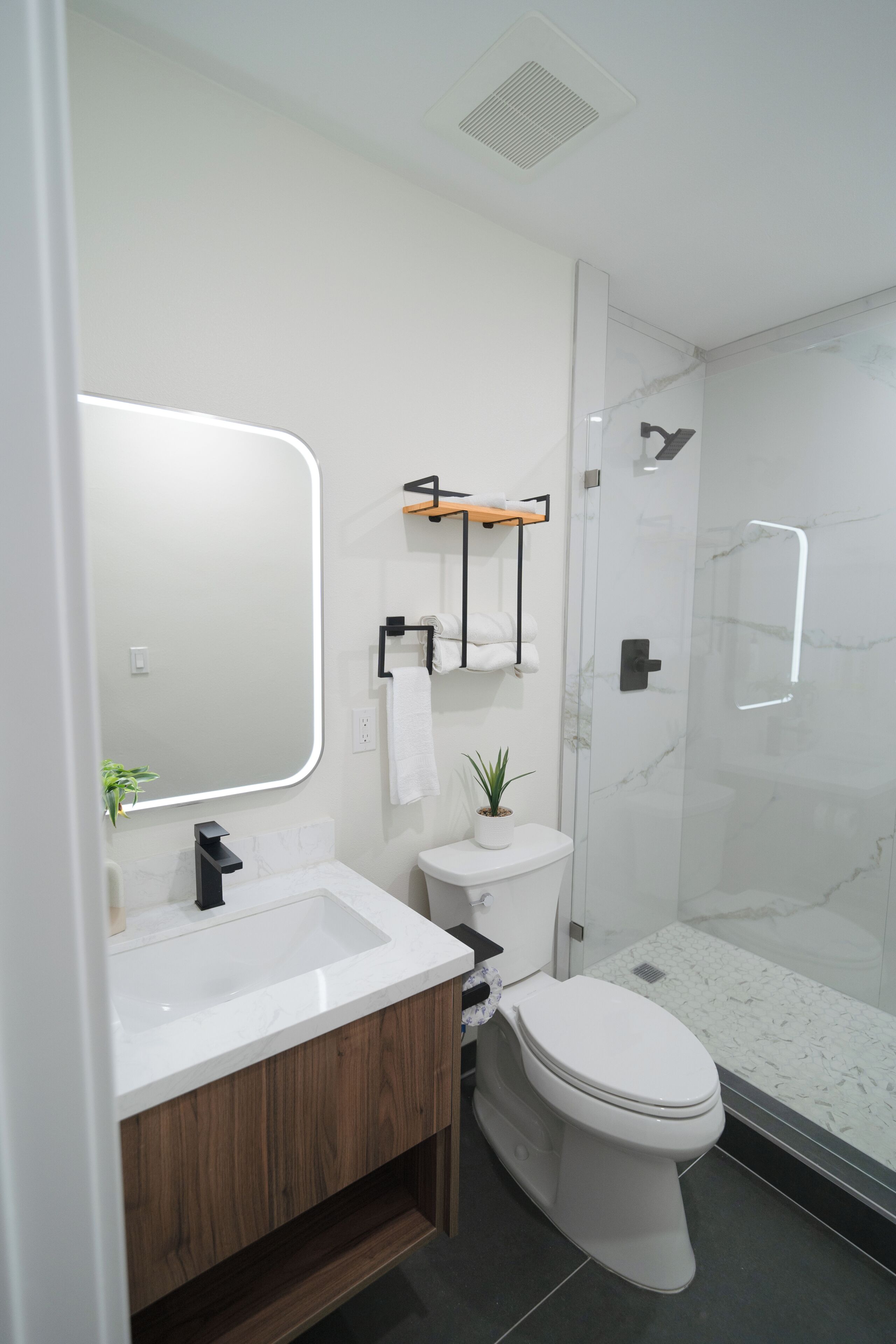 A modern bathroom with a white sink, wooden vanity, a toilet, a glass shower enclosure, and a large mirror.