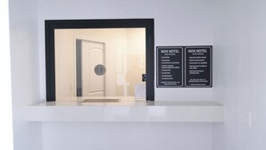 A hotel reception area with a white counter, a door leading to the rooms, and two signs with hotel policies. - Nox Hotel - Studio City (Studio City)
