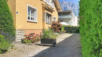 Un sentier pavé de pierres menant à un bâtiment jaune orné de détails en pierre, doté d’un balcon et offrant une vue sur la montagne.