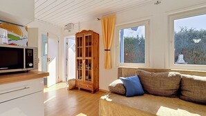 Una stanza con un armadio in legno, un divano con cuscini, un forno a microonde e una finestra vista alberi.