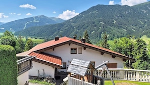 Un hôtel offrant une vue sur la montagne, avec un bâtiment à toit rouge, un balcon en bois et une vue sur des montagnes verdoyantes.