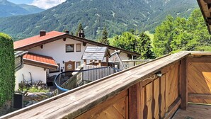 Un balcon en bois offrant une vue sur une montagne et un bâtiment avec un toit rouge.
