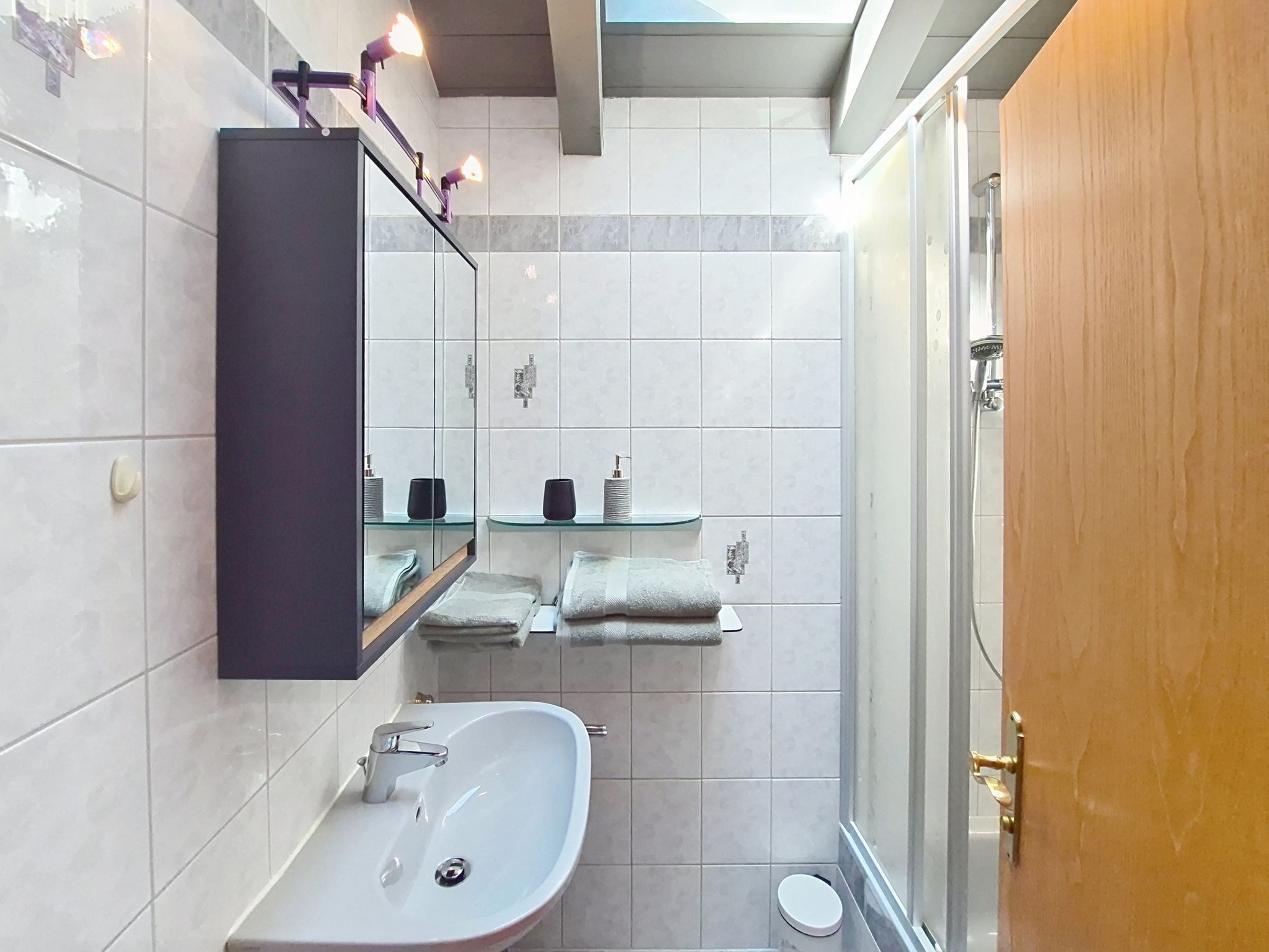 Une salle de bain équipée d’un lavabo, d’un miroir, d’étagères contenant des articles de toilette et d’un espace douche.