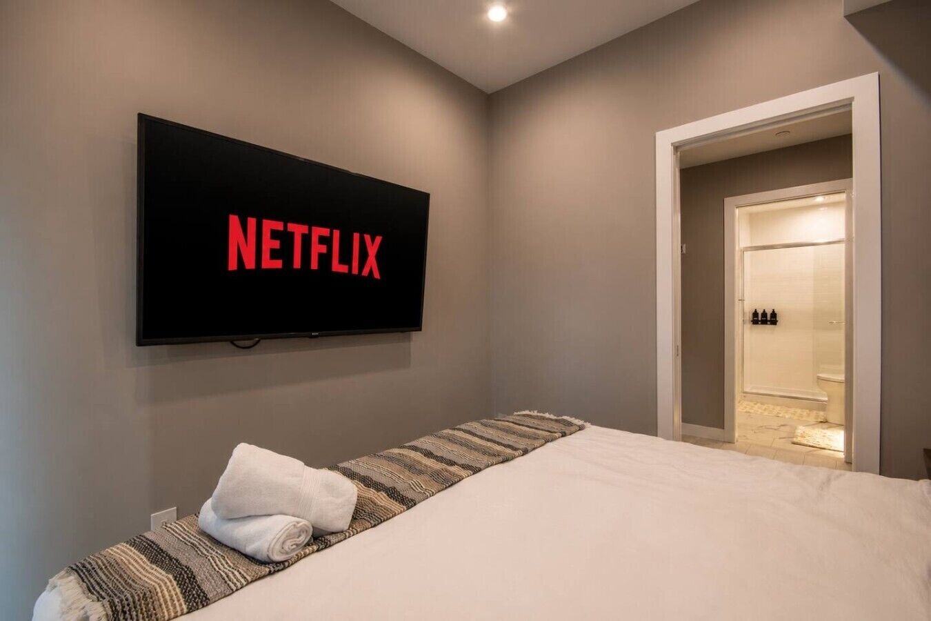 Un dormitorio con cama, un televisor mostrando 'NETFLIX' y un rincón con ducha.