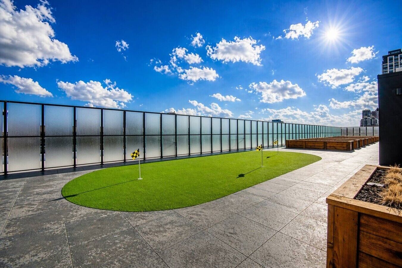 A rooftop with a green artificial turf area, a checkered flag, and a glass fence.