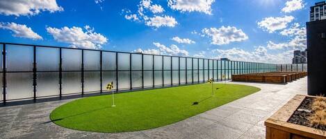 A rooftop with a green artificial turf area, a checkered flag, and a glass fence.