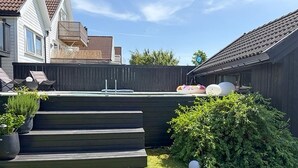 Een achtertuin met een houten terras, een klein zwembad en een verzorgd gazon.