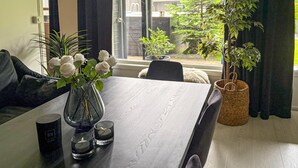 Een eettafel met een vaas witte rozen, twee kaarsen en een zwarte mok.