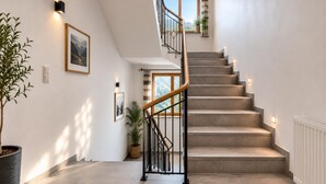 A staircase with a wooden handrail and black railings, leading to a landing with a window and a potted plant. - Modern vacation home near the gondolas (Kirchberg in Tirol)