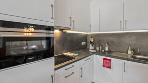 Una cocina moderna con armarios blancos, horno integrado, cafetera y pileta de acero inoxidable.
