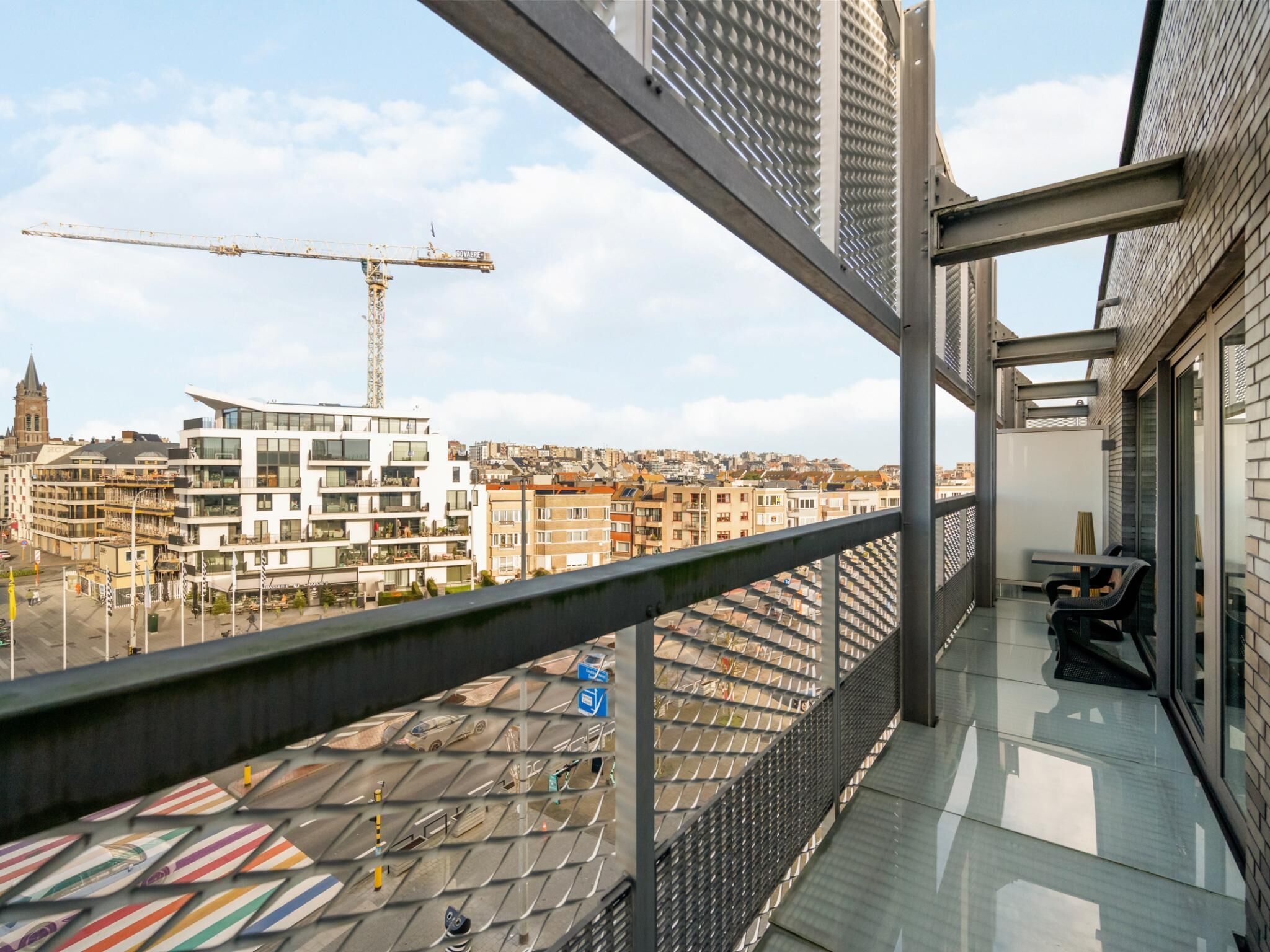 Un balcon offrant une vue sur le paysage urbain, avec notamment une grue de construction et des bâtiments modernes.