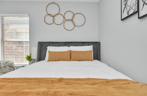 A bedroom with a bed, a window with blinds, a wall-mounted Olympic rings decoration, and a plant.