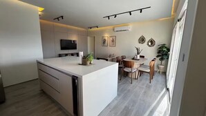 Eine moderne Küche mit einer zentralen Kochinsel, einem Essbereich mit rundem Tisch und Stühlen sowie einem an der Wand befestigten Flachbildfernseher.