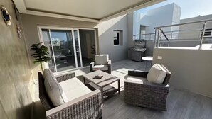 Ein Balkon mit Korbmöbeln, einem Grill und einer Schiebetür.