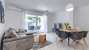 Un soggiorno moderno con un divano grigio, un tavolo da pranzo con sedie, una TV e un'ampia finestra con tende.