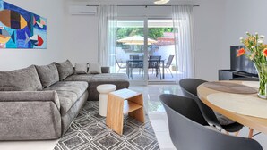 Un soggiorno moderno con un divano componibile, un tavolino in legno, un'area da pranzo con un tavolo rotondo e sedie, e un'ampia finestra con tende.