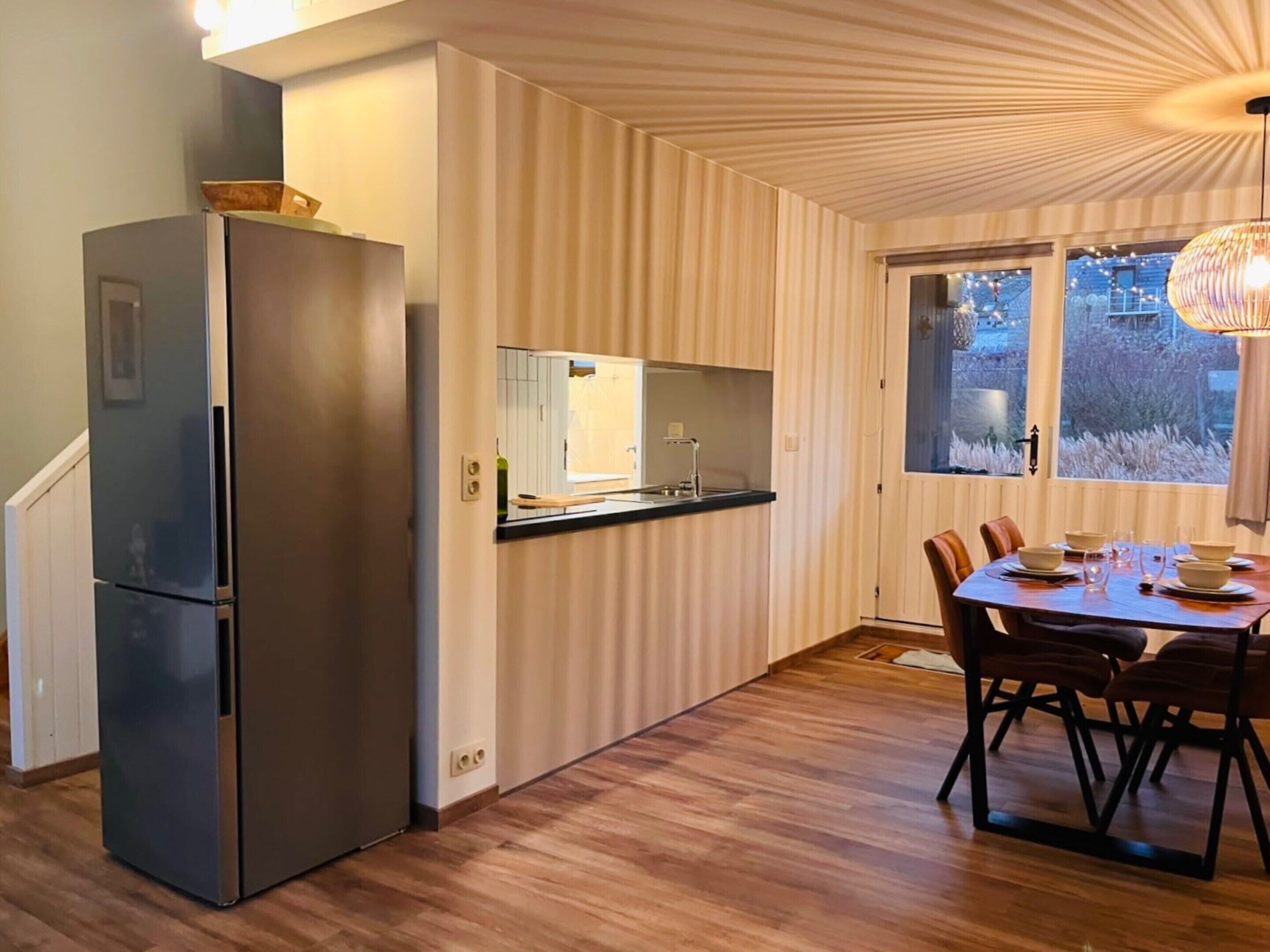 Ett kompakt kök med ett inbyggt kylskåp, en liten arbetsbänk och en matplats med ett bord och stolar.