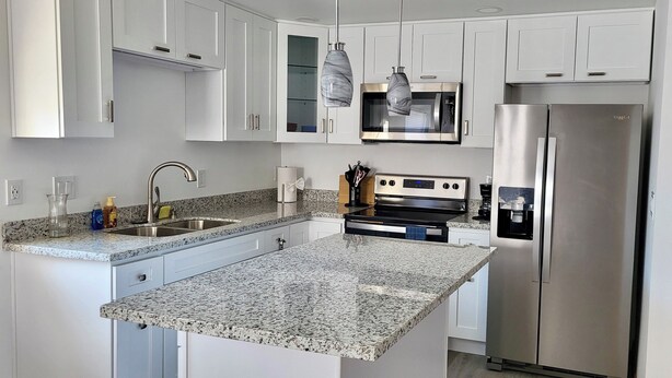 Cocina moderna con armarios blancos, encimeras de granito, electrodomésticos de acero inoxidable e iluminación colgante.