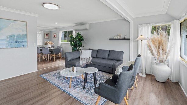 Ein modernes Wohnzimmer mit einem grauen Sofa, zwei Sesseln, einem Couchtisch und einem Essbereich im Hintergrund.