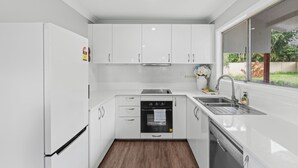 Eine moderne Küche mit weißen Schränken, Backofen, Geschirrspüler und einem Fenster mit Blick ins Grüne.
