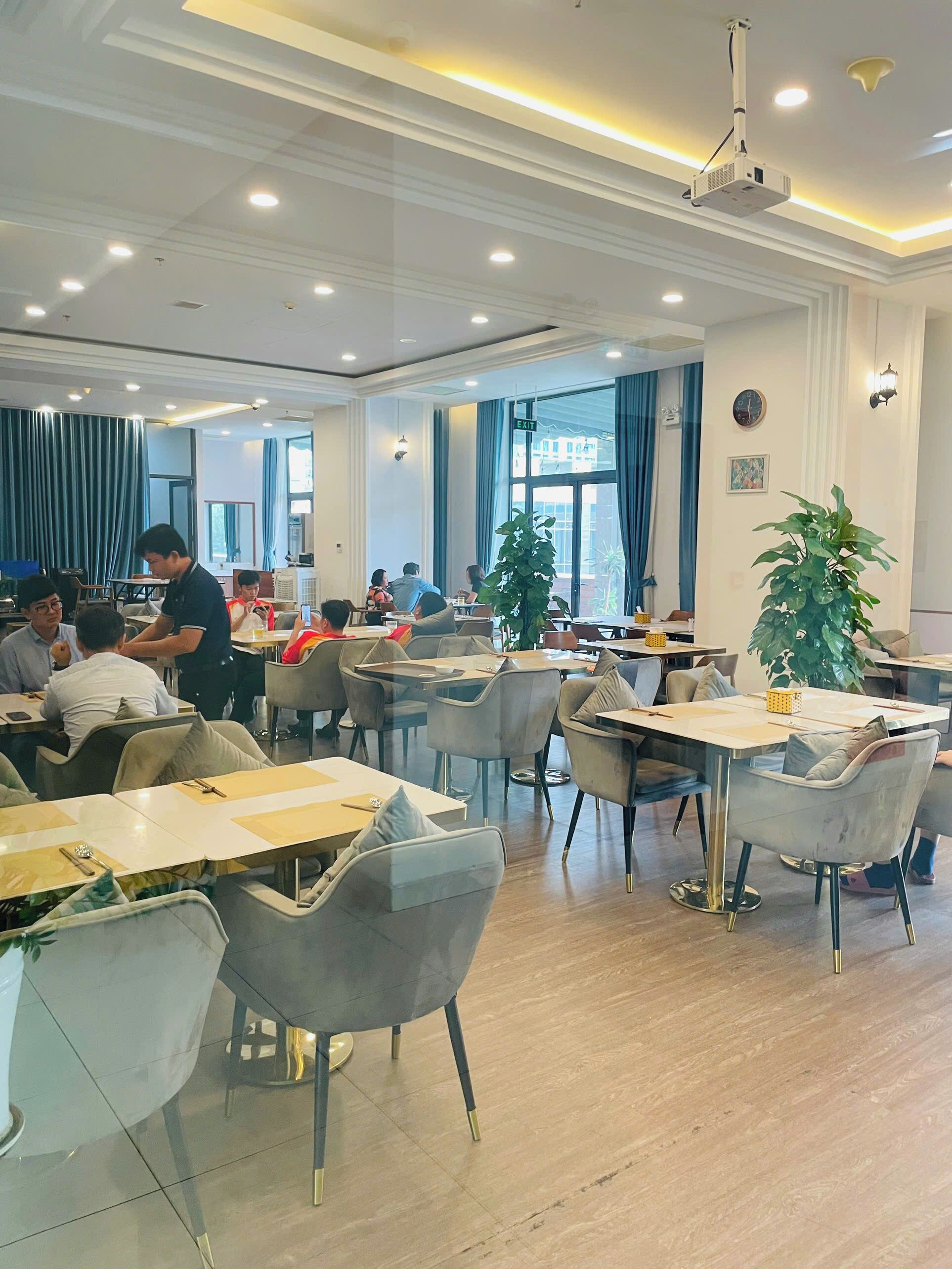A spacious dining area with tables and chairs, a projector, and large windows.