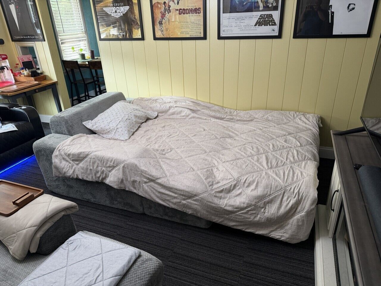 Un letto singolo con copriletto trapuntato, un comodino, una sedia e un tavolino con vassoio.