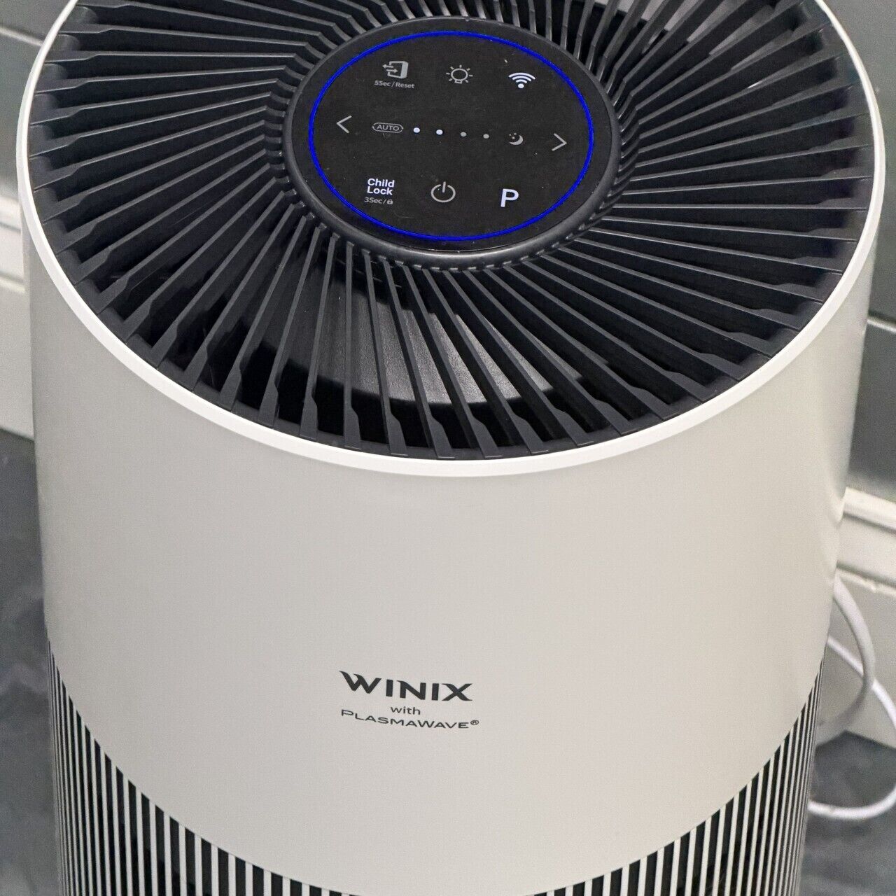 Un purificateur d’air blanc doté d’un panneau de commande circulaire bleu, portant l’inscription « WINIX avec PLASMAWAVE ».