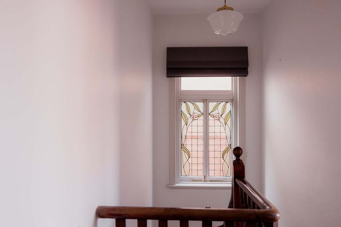 Une pièce dotée d’une fenêtre ornée de vitraux, d’un escalier en bois et d’un luminaire au plafond.
