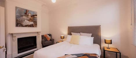 Ett hotellrum med en stor säng, en öppen spis, en tavla på väggen och två sänglampor.