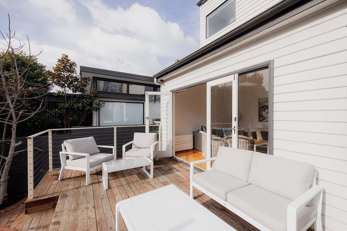 Une terrasse extérieure moderne, dotée de meubles blancs, notamment des canapés et des fauteuils, et d’un plancher en bois.