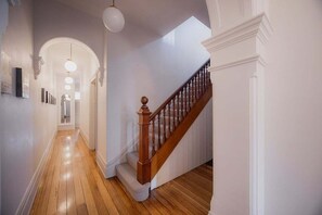 A hallway with wooden flooring, a staircase with a wooden handrail, and a white wall with a decorative molding.