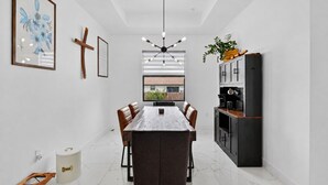 A modern kitchen with a dining area, featuring a marble floor, pendant lighting, and a view through a window.