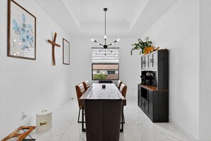 Een moderne keuken met een eetgedeelte, met een marmeren vloer, hanglampen en uitzicht door een raam.