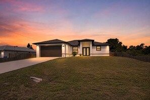 Een modern, gelijkvloers huis met garage, een verzorgd gazon en een heldere lucht in de schemering.