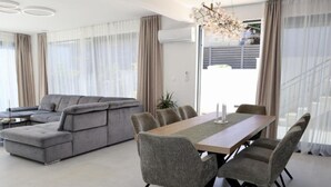 A modern living room with a grey sectional sofa, a dining table with grey chairs, and a chandelier. - Sunset Villa Aves With Pool, Gym and Sauna - Four Bedroom Villa (Rogac)