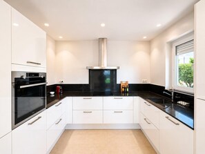 A modern kitchen with white cabinets, black countertops, a stainless steel range hood, and a window providing a view. - Villa Belleza - Santa Cristina d'Aro, Catalonia (Santa Cristina d'Aro)